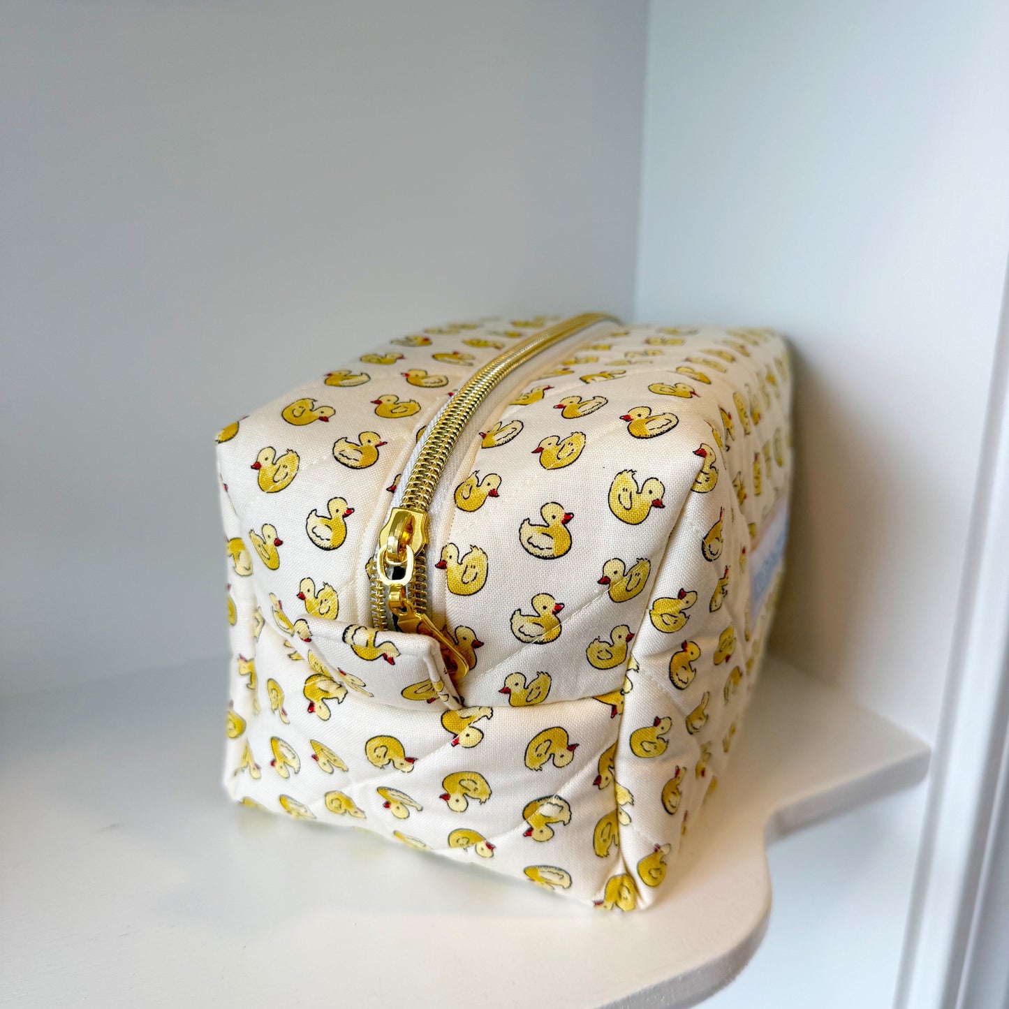 Cosmetic bag with duck pattern on a white shelf