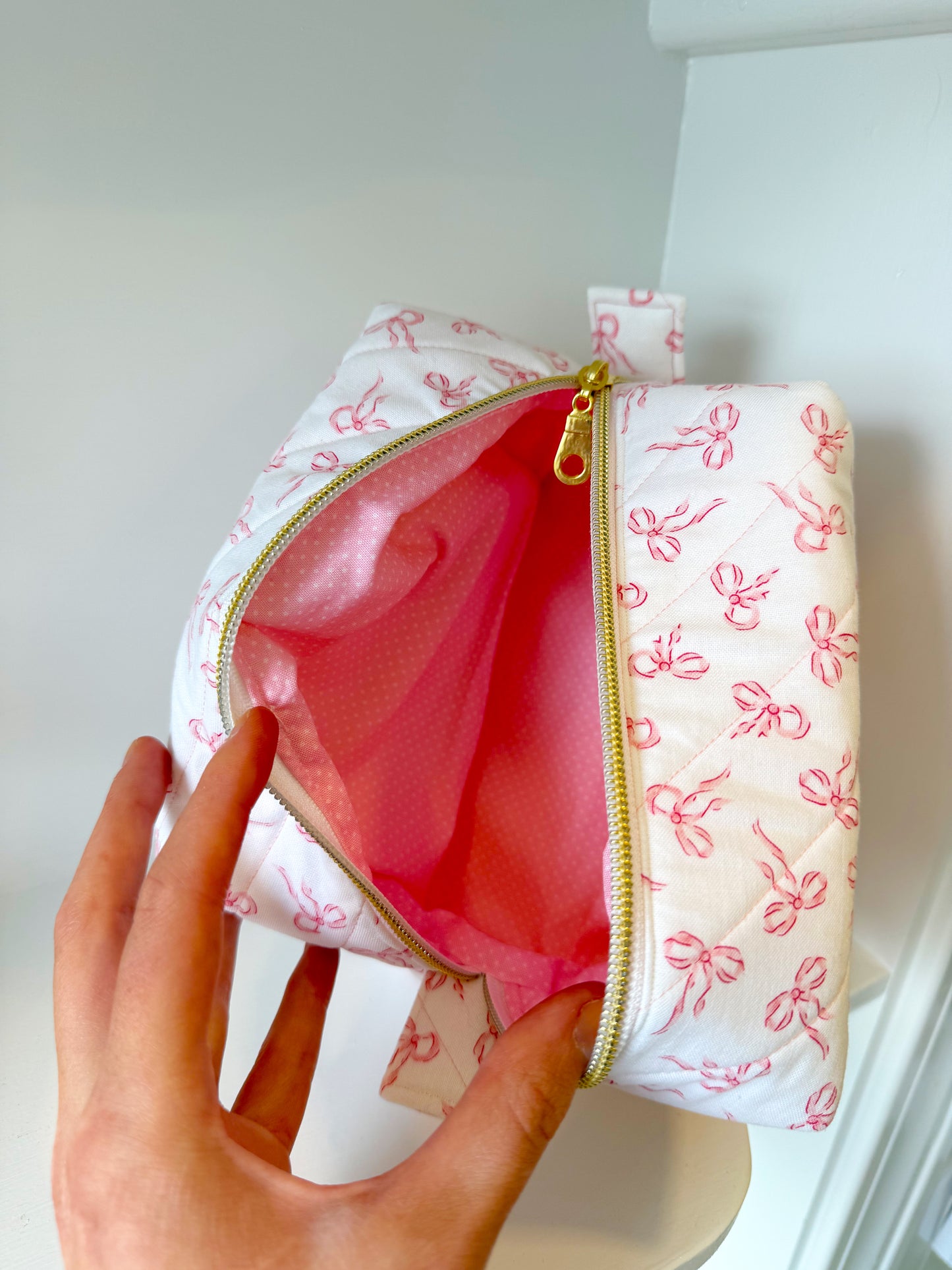 Small pouch with pink interior and bow pattern on a white background