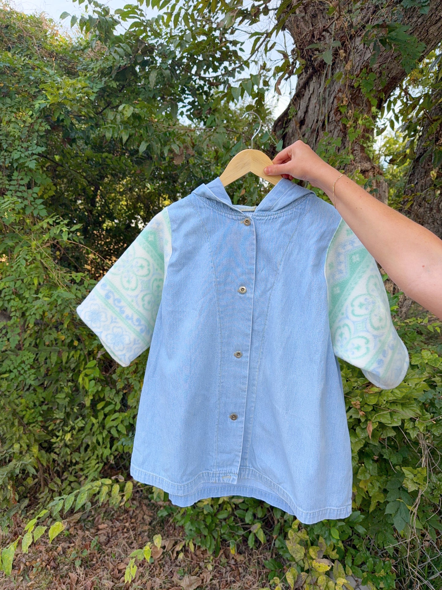 Light blue denim shirt with patterned sleeves on a hanger against a natural background